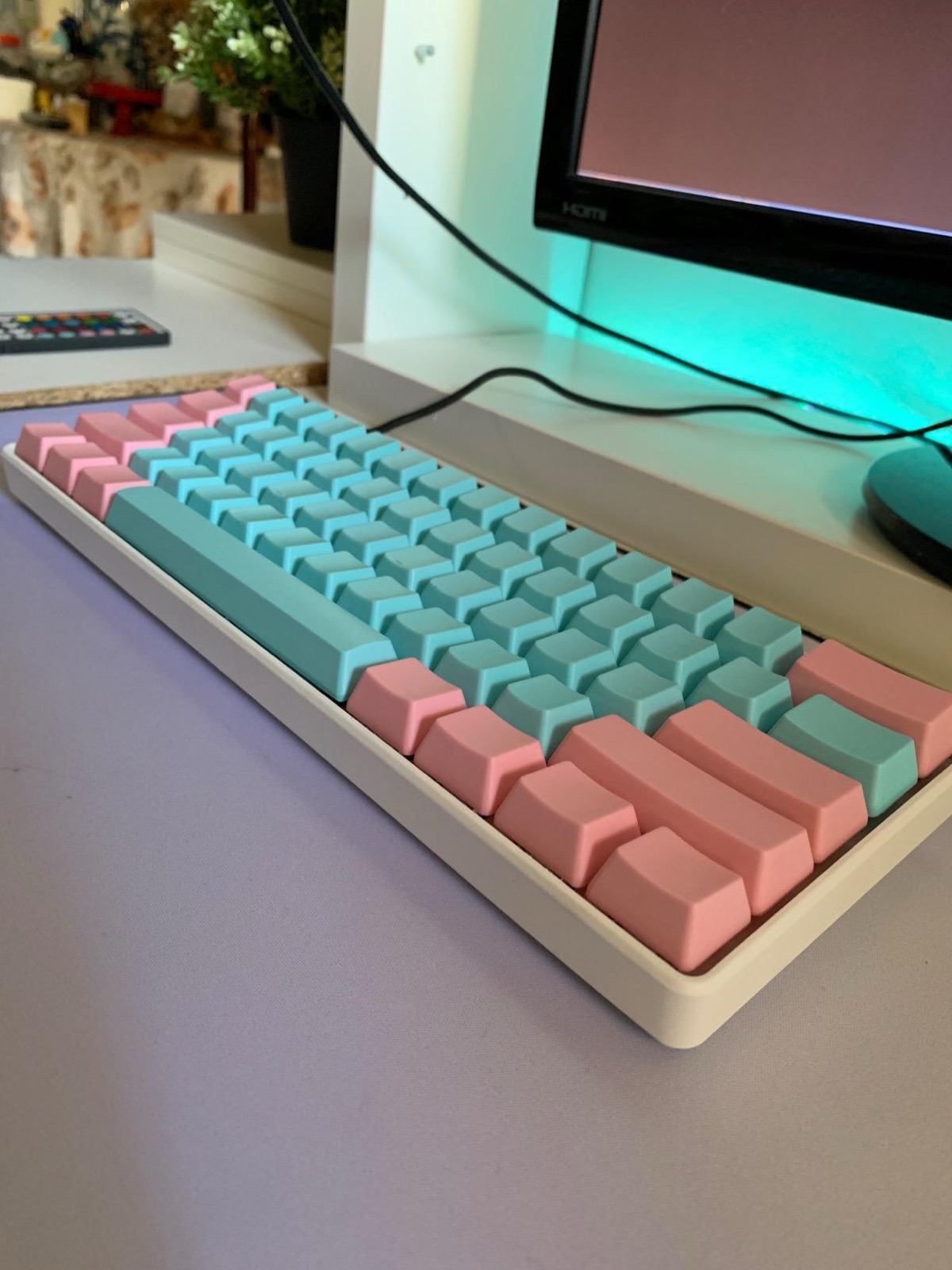 GK61 with pastel pink and teal custom keycaps on a white desk under a monitor